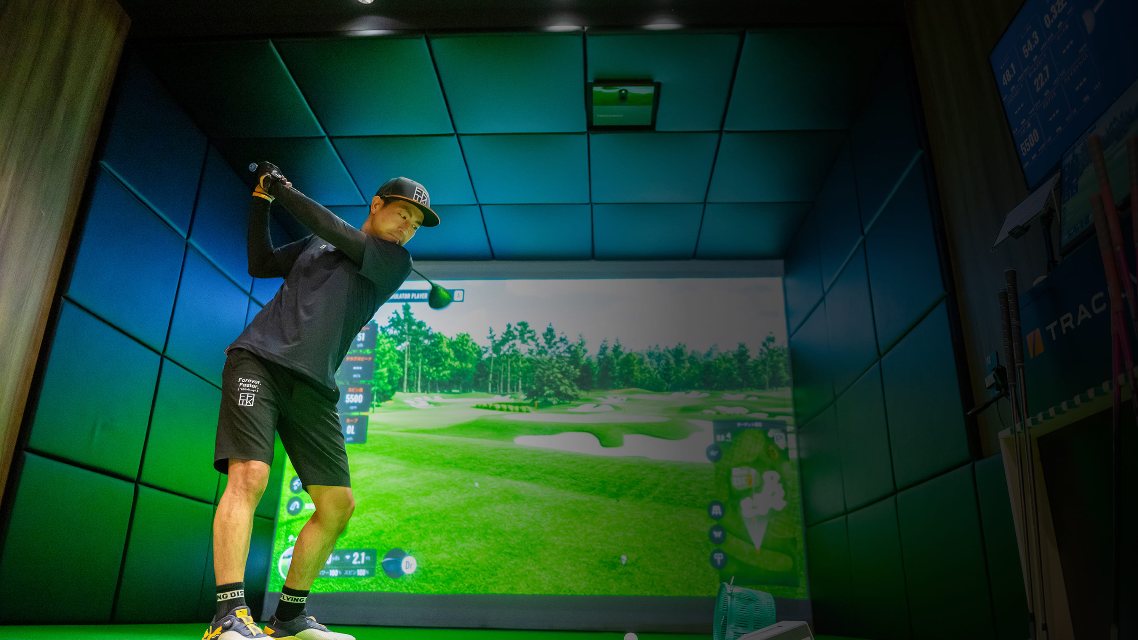 バーチャルコース画面付きインドアゴルフシミュレーターでスイングするゴルファー