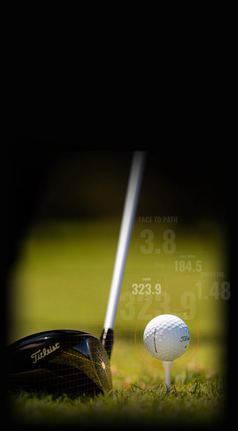 Golf club poised to hit a ball on a tee, with performance stats overlayed, including distance and speed metrics, on a grassy course.